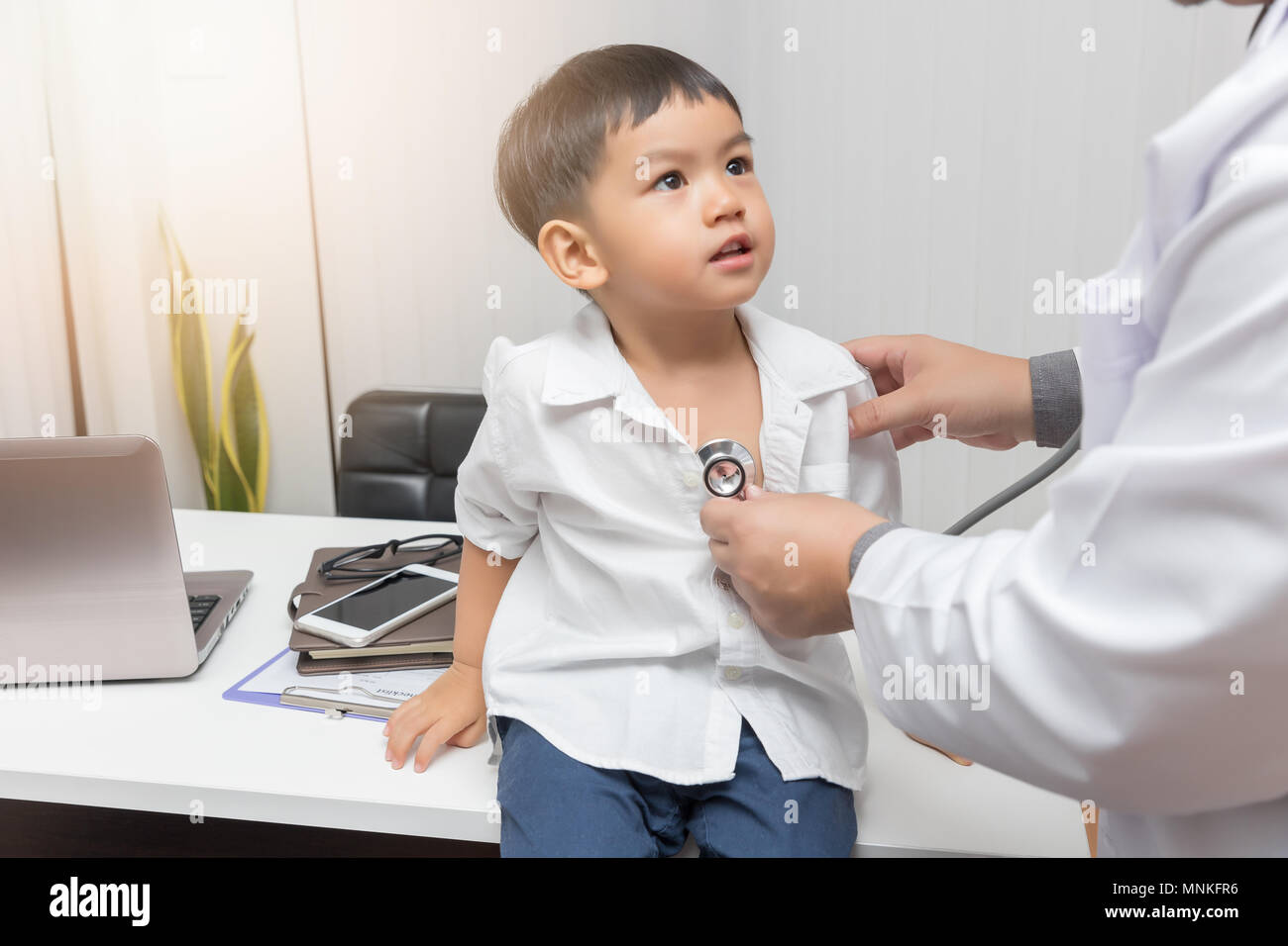 Pediatrician doctor examining a little asian boy by stethoscope Stock Photo