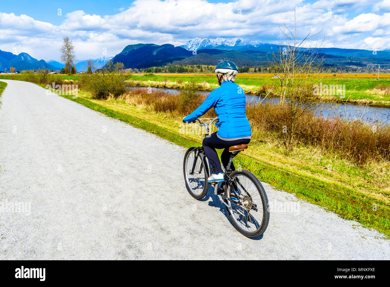 Landscape scenery with the Coast Mountains and the South Alouette River while biking the dyke at Pitt Polder at Pitt Meadows, BC, Canada Stock Photo