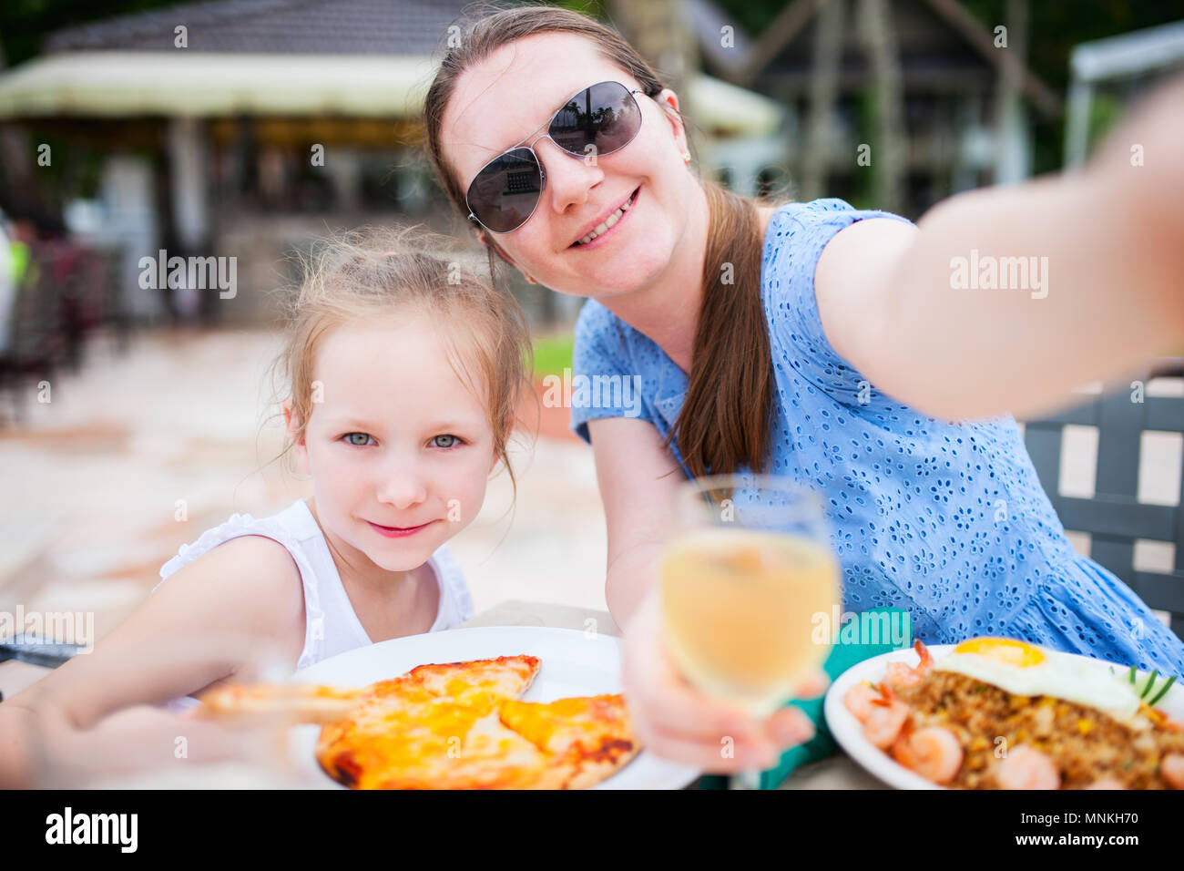 Happy mother and her adorable little daughter at outdoors restaurant taking selfie while having