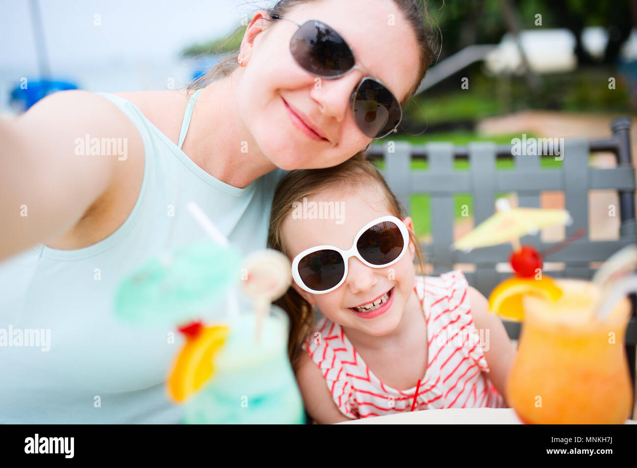 Happy mother and her adorable little daughter at outdoors cafe taking selfie while drinking tropical juice Stock Photo
