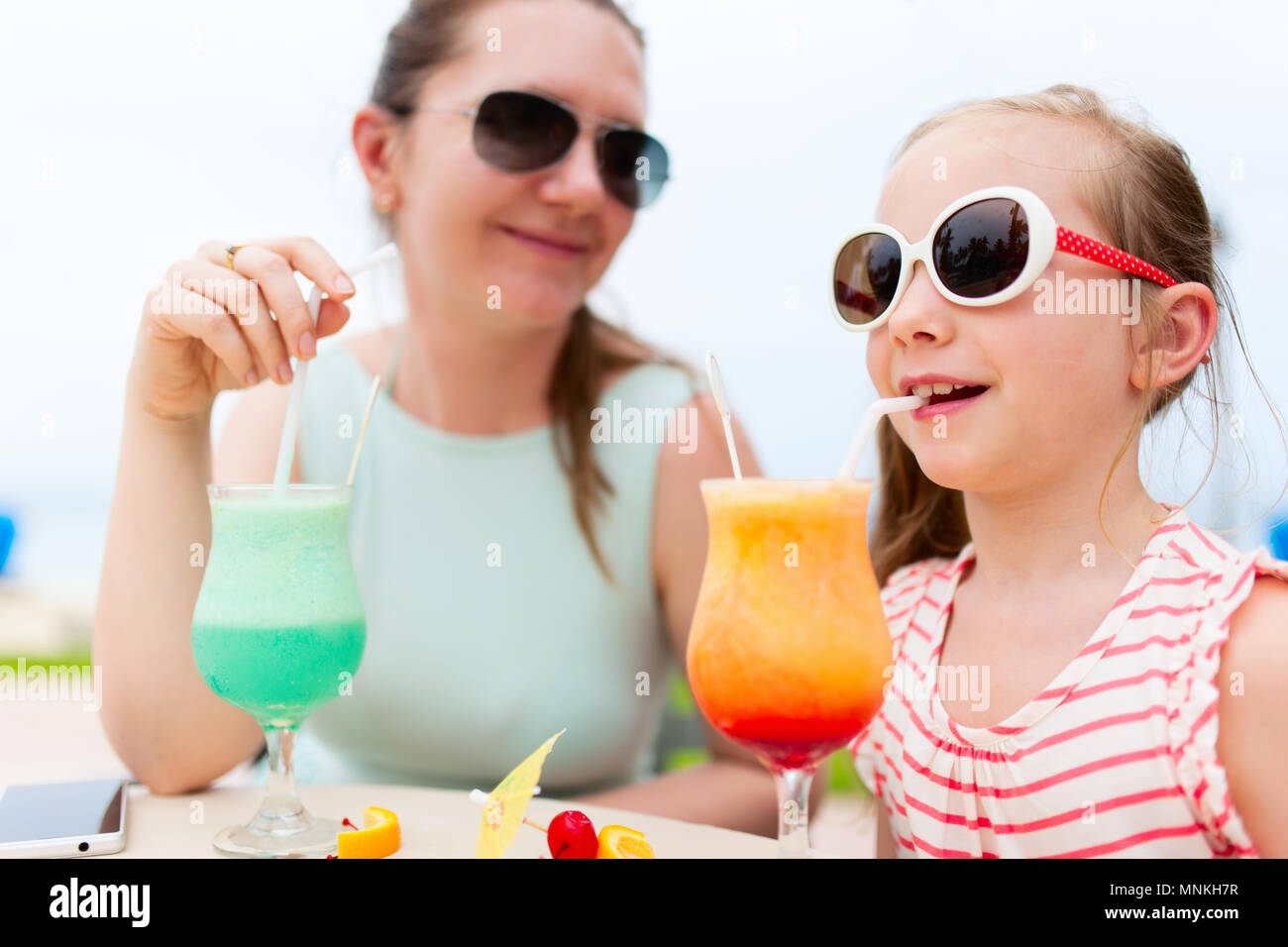 Happy mother and her adorable little daughter at outdoors cafe drinking tropical juice Stock Photo
