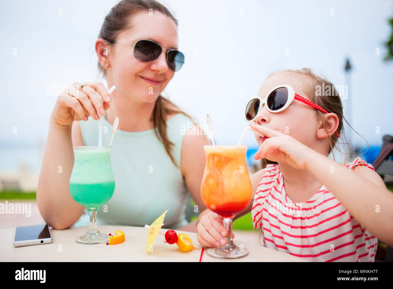 Happy mother and her adorable little daughter at outdoors cafe drinking tropical juice Stock Photo