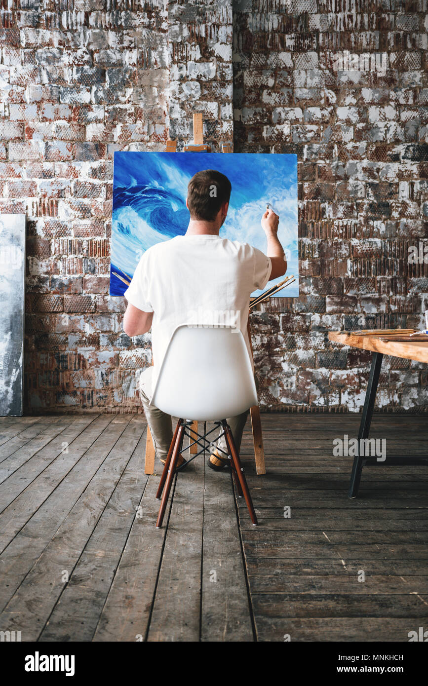 Artist is paint an oil painting in art studio while sitting on a chair