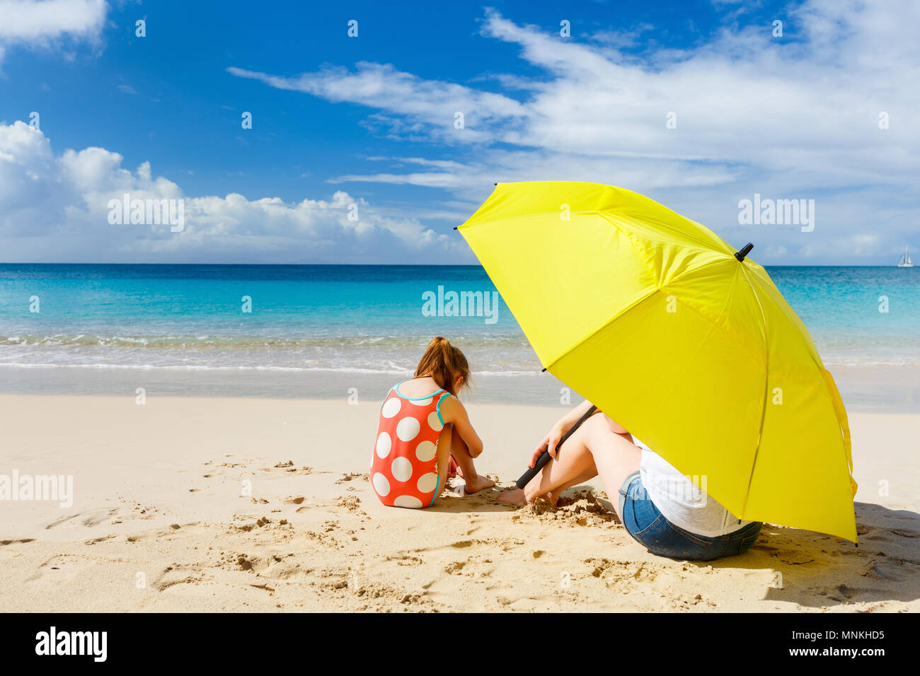 Mother and daughter with big yellow umbrella hiding from sun at