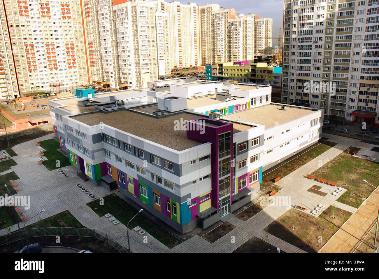 школа рядом с домом. жилой комплекс с детским садом. сад с газоном и деревьями. клумбы возле подъезда. детский сад рядом с домом.