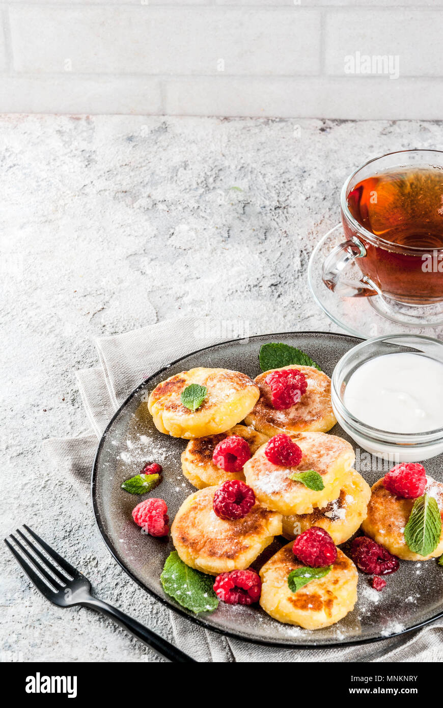 Healthy summer breakfast, cheese pancakes with raspberry, powdered sugar and mint, grey concrete background copy space Stock Photo