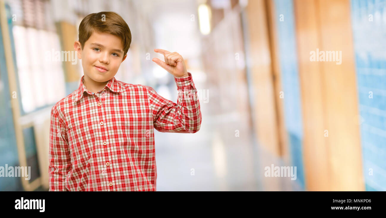 Handsome toddler child with green eyes holding something very tiny, size concept at school corridor Stock Photo