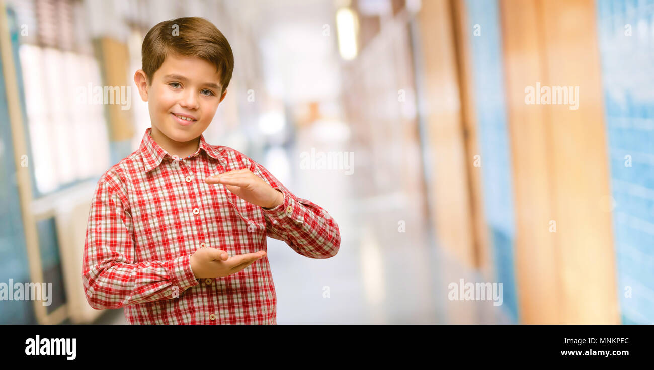 Handsome toddler child with green eyes holding something, size concept at school corridor Stock Photo