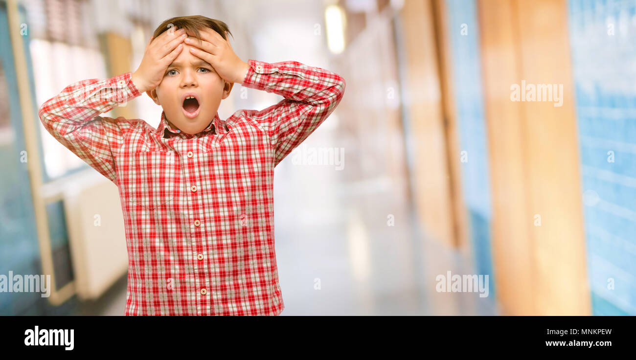 Handsome toddler child with green eyes stressful keeping hands on head, terrified in panic, shouting at school corridor Stock Photo