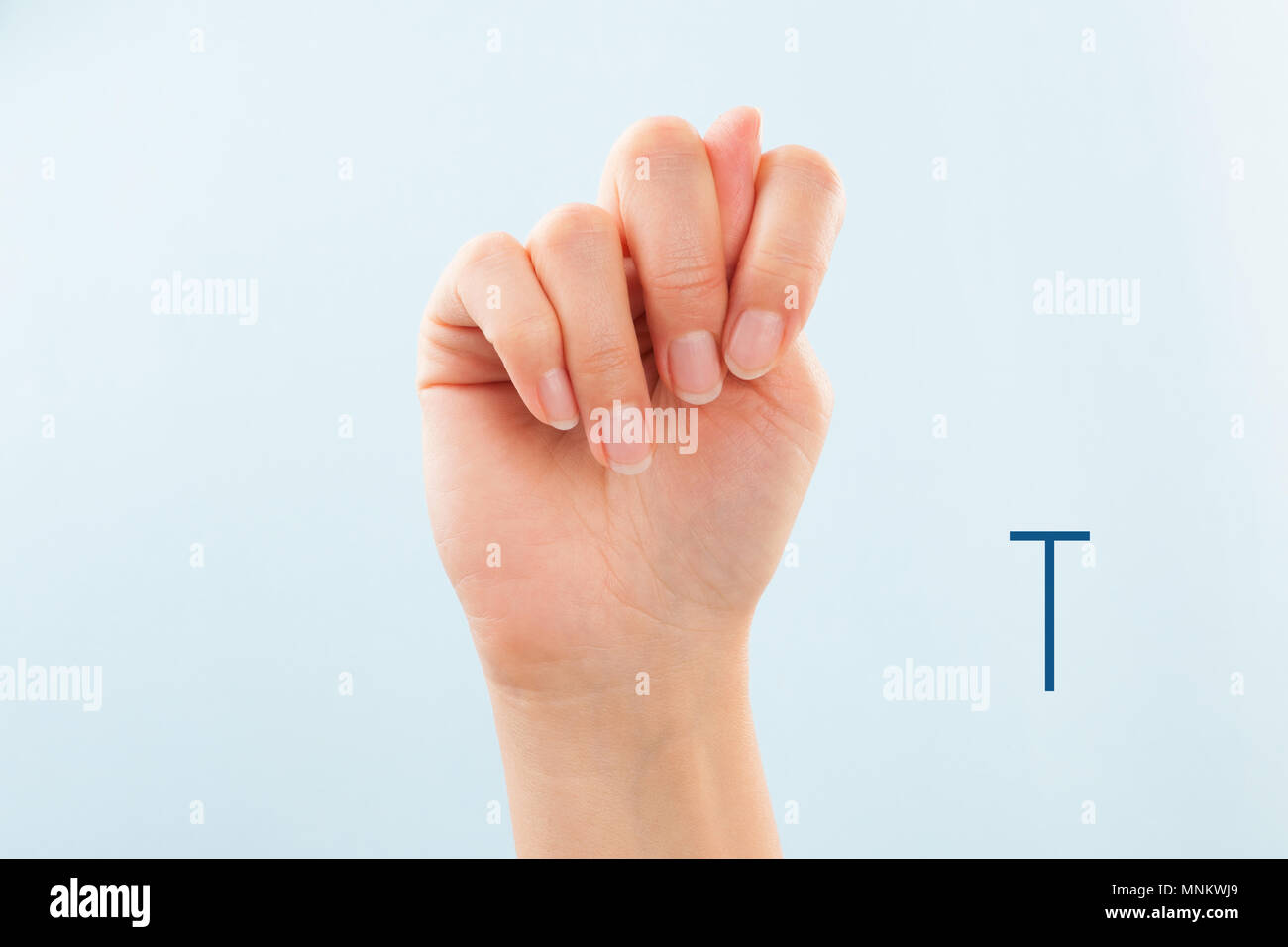 American sign language. Female hand showing letter T isolated on blue background. Stock Photo