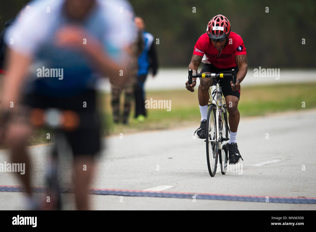 A U.S. Marine crosses the finish line during the 2018 Marine Corps Trials cycling competition at Marine Corps Base Camp Lejeune, N.C., March 18, 2018. The Marine Corps Trials promotes recovery and rehabilitation through adaptive sport participation and develops camaraderie among recovering service members (RSMs) and veterans. It is an opportunity for RSMs to demonstrate their achievements and serves as the primary venue to select Marine Corps participants for the DoD Warrior Games. Stock Photo