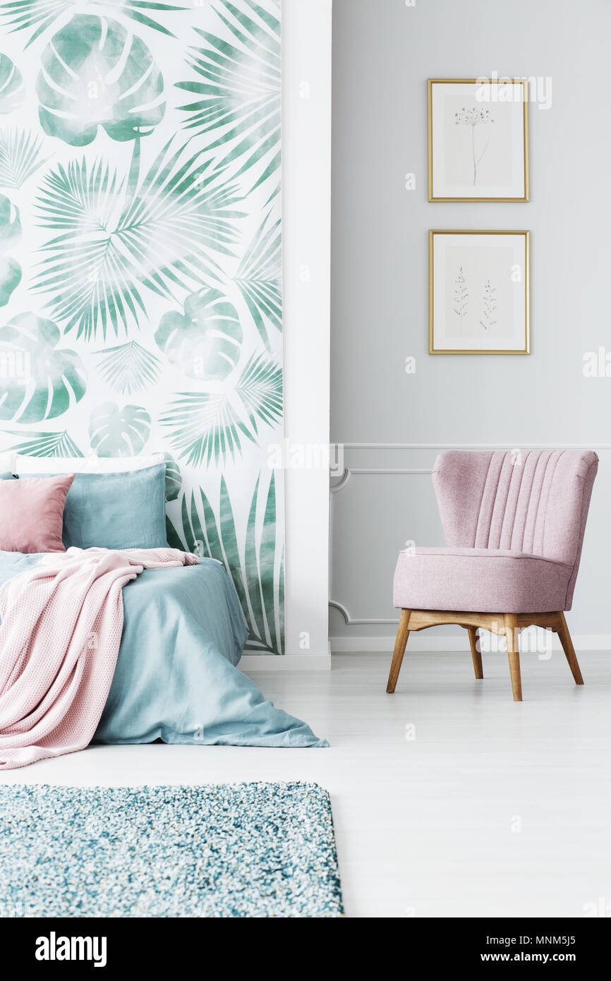 Powder pink armchair standing in bedroom interior with leaf wallpaper