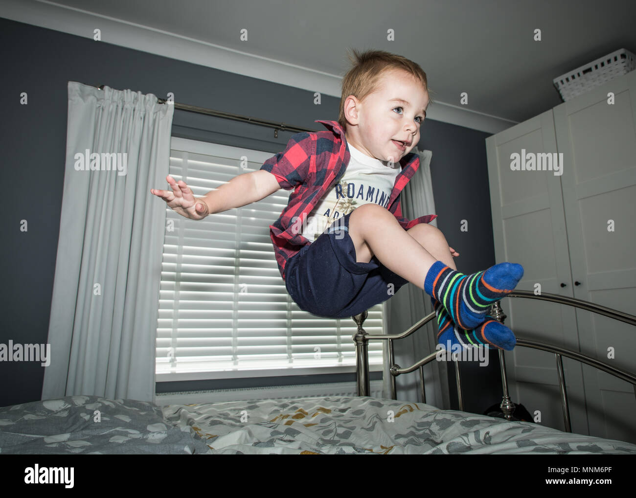 A little boy jumps on a bed in a bedroom / Child jumping on bed Stock Photo