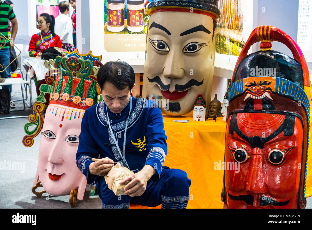China artisan, craftsman, carving colorful wood Chinese masks of varying sizes at a culture fair in Shenzhen China Stock Photo