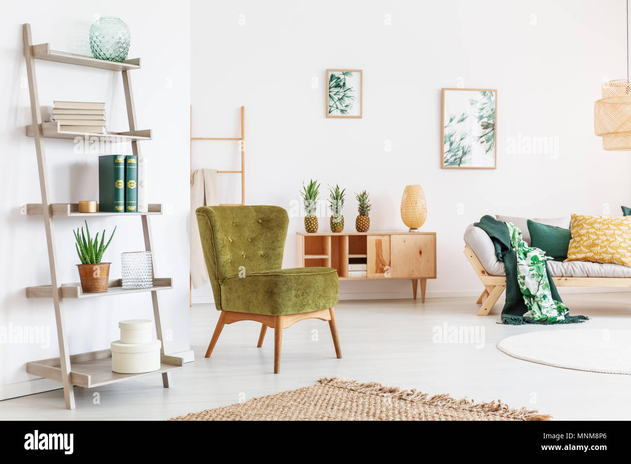 Pear green chair and yellow pillow on beige sofa in cozy room with accessories on wooden shelf Stock Photo