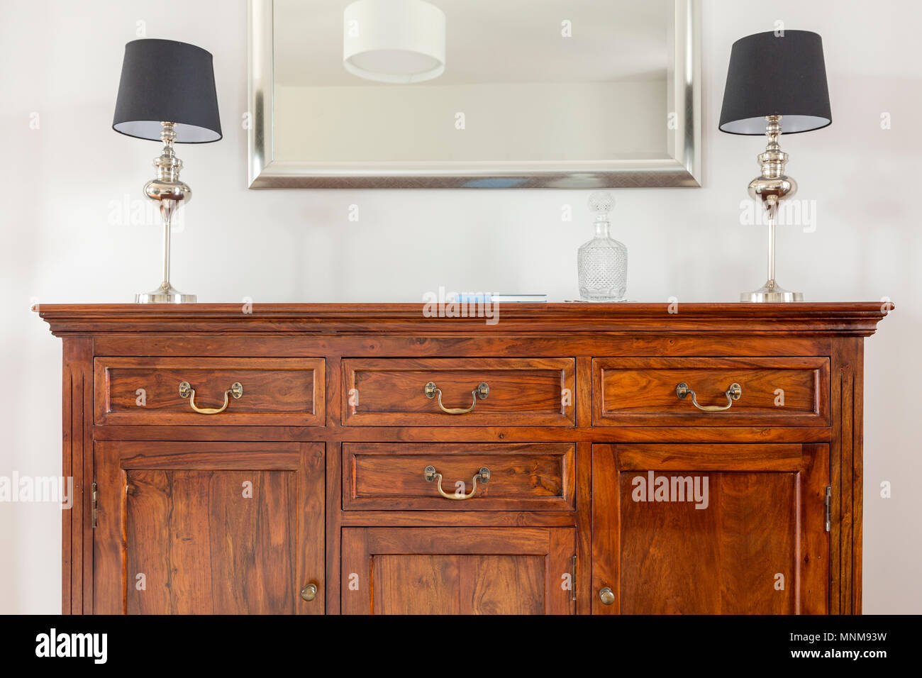 Stylish wooden dresser, two small lamps and mirror in a modern frame
