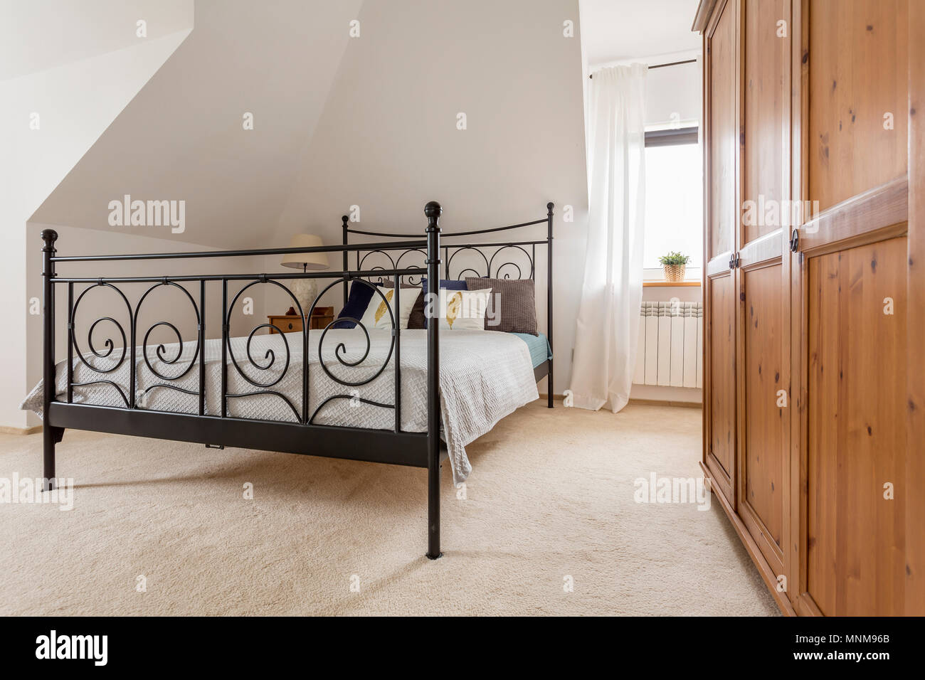 Light bedroom with wooden wardrobe and bed with decorative metal frame Stock Photo