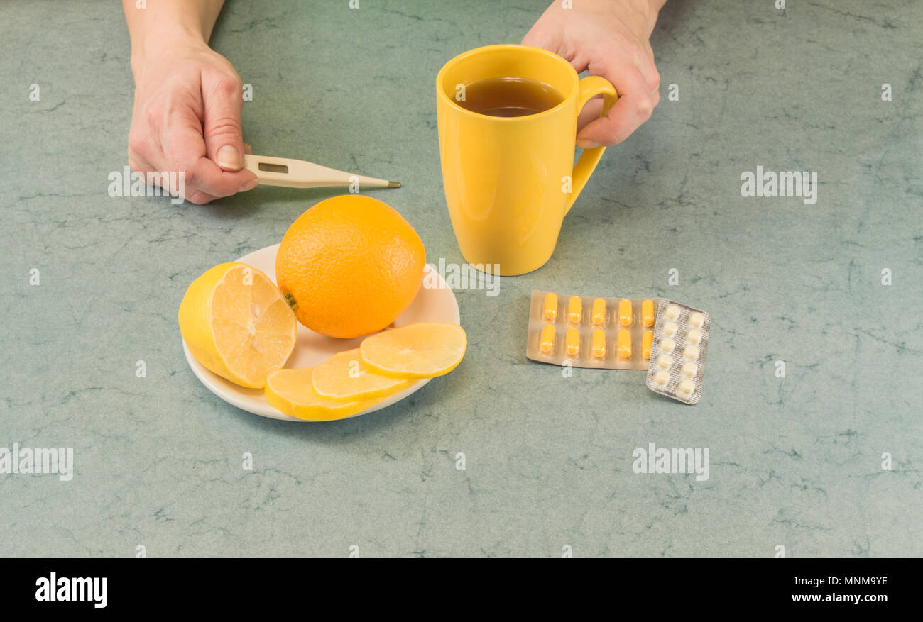 Sick person who is looking at thermometer and drinking hot tea with lemon Stock Photo Alamy