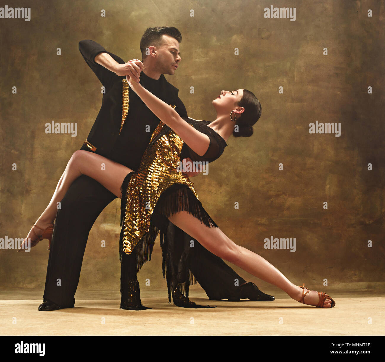 Dance ballroom couple in gold dress dancing on studio background. Stock Photo