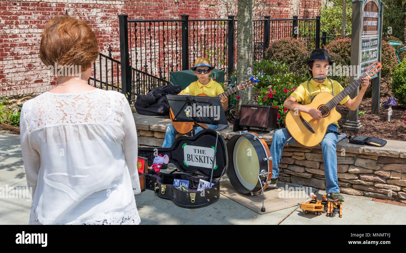 Two young boys busking with guitars on Main street in Blowing Rock, NC, USA, being watch by a red-haired woman bystander. Stock Photo