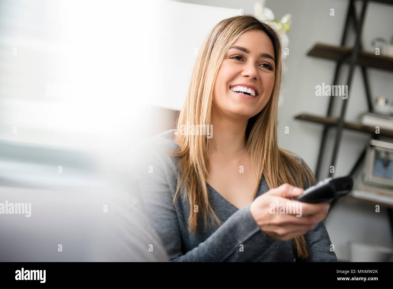 Young woman watching tv and laughing Stock Photo