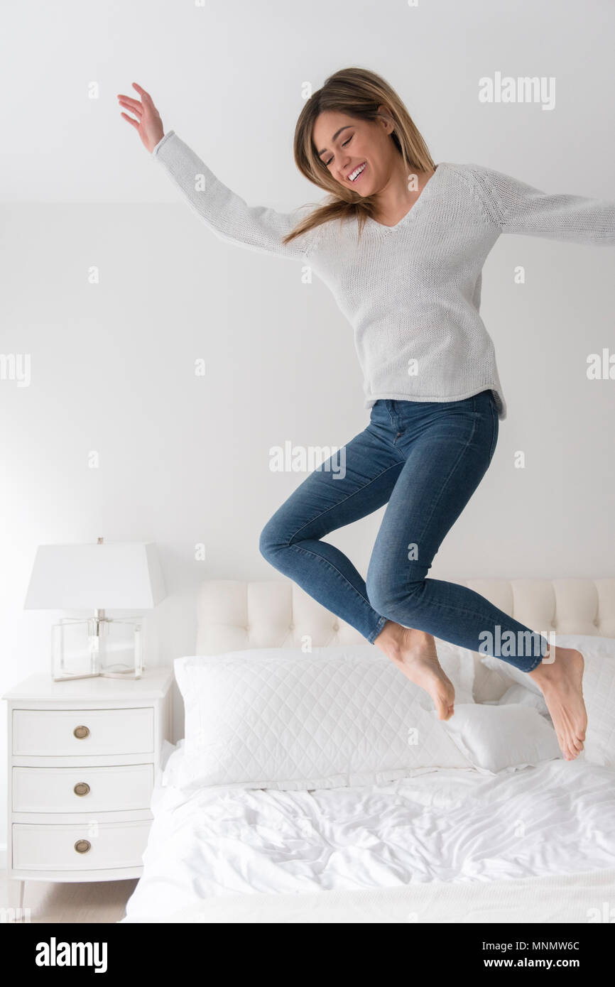 Young woman jumping in bedroom Stock Photo