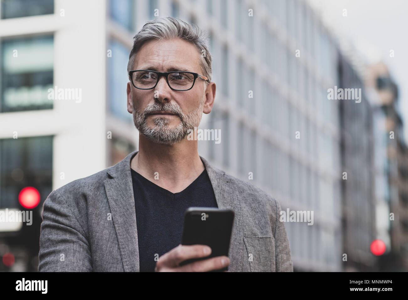 Mature male walking and on on smartphone in city Stock Photo