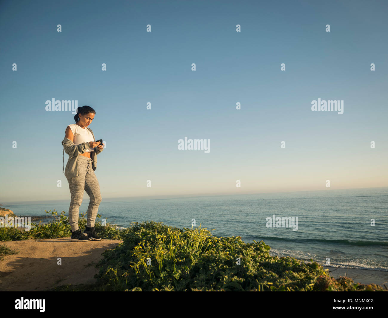 USA, California, Newport Beach, Woman standing on cliff and looking at phone Stock Photo