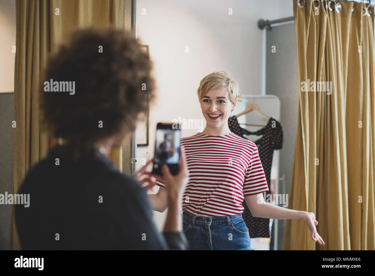 Young adult female trying on clothes in a vintage store with friend Stock Photo