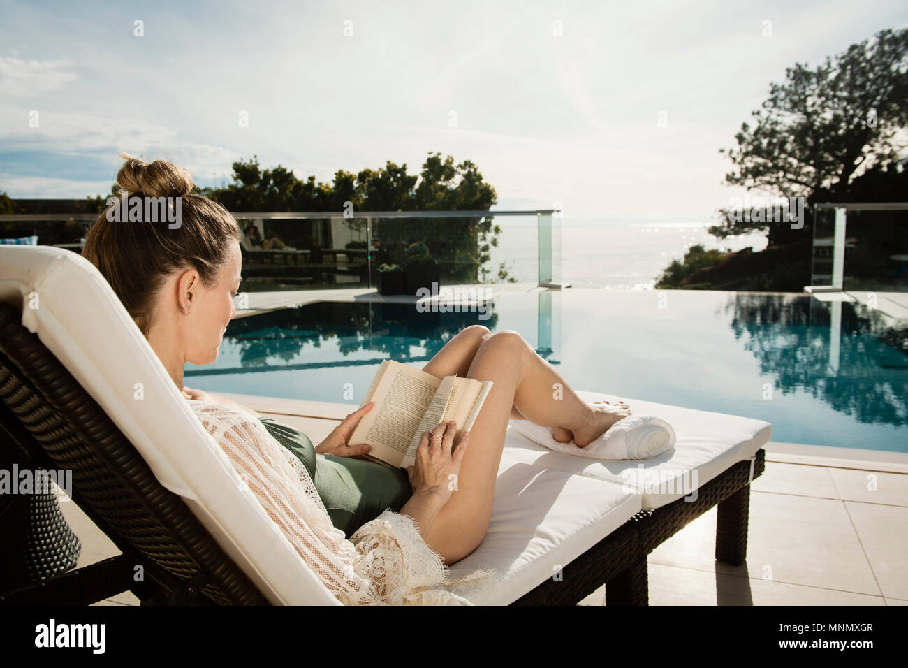 Woman reading book by swimming pool Stock Photo