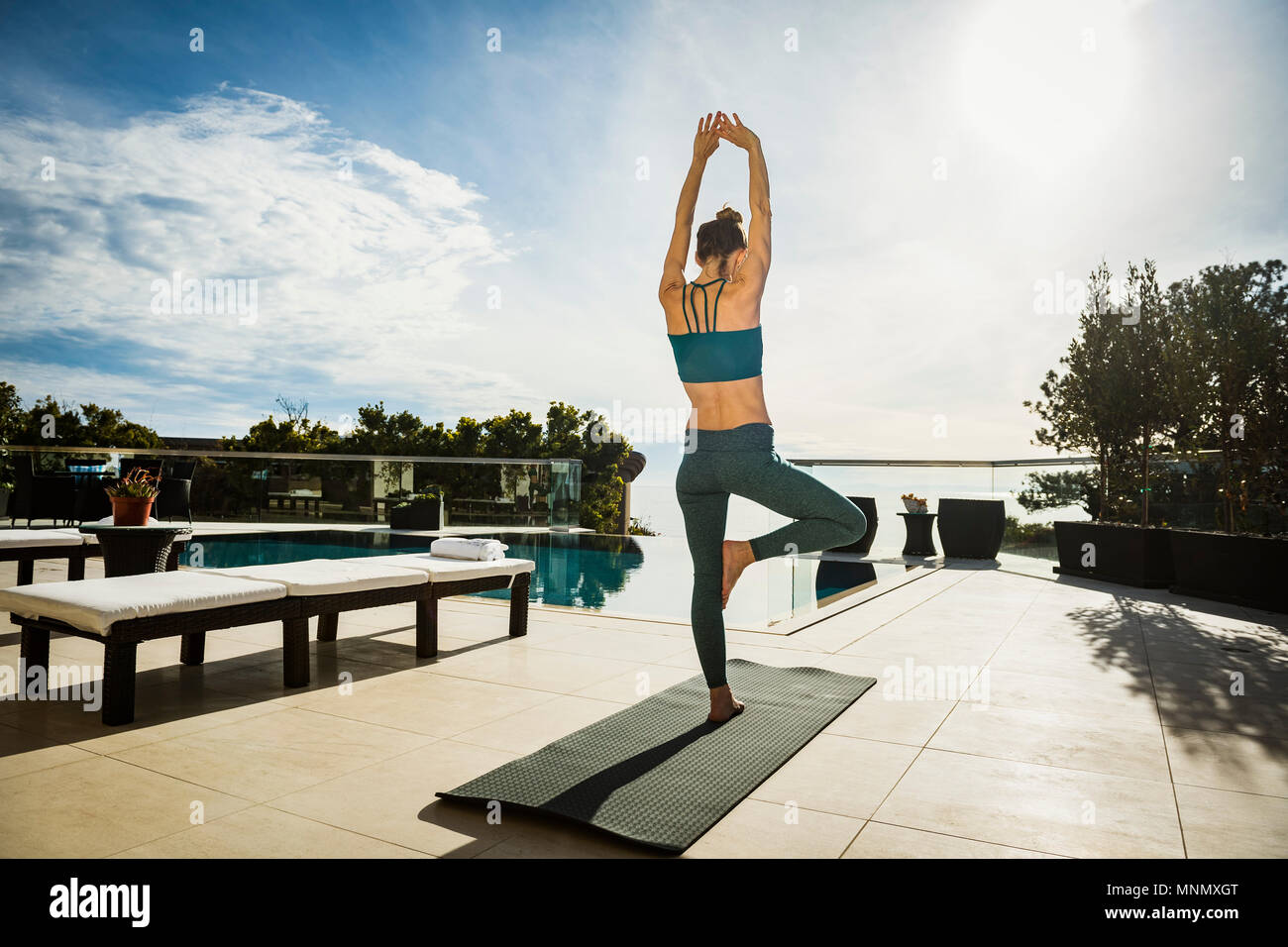 Woman practicing yoga by swimming pool Stock Photo