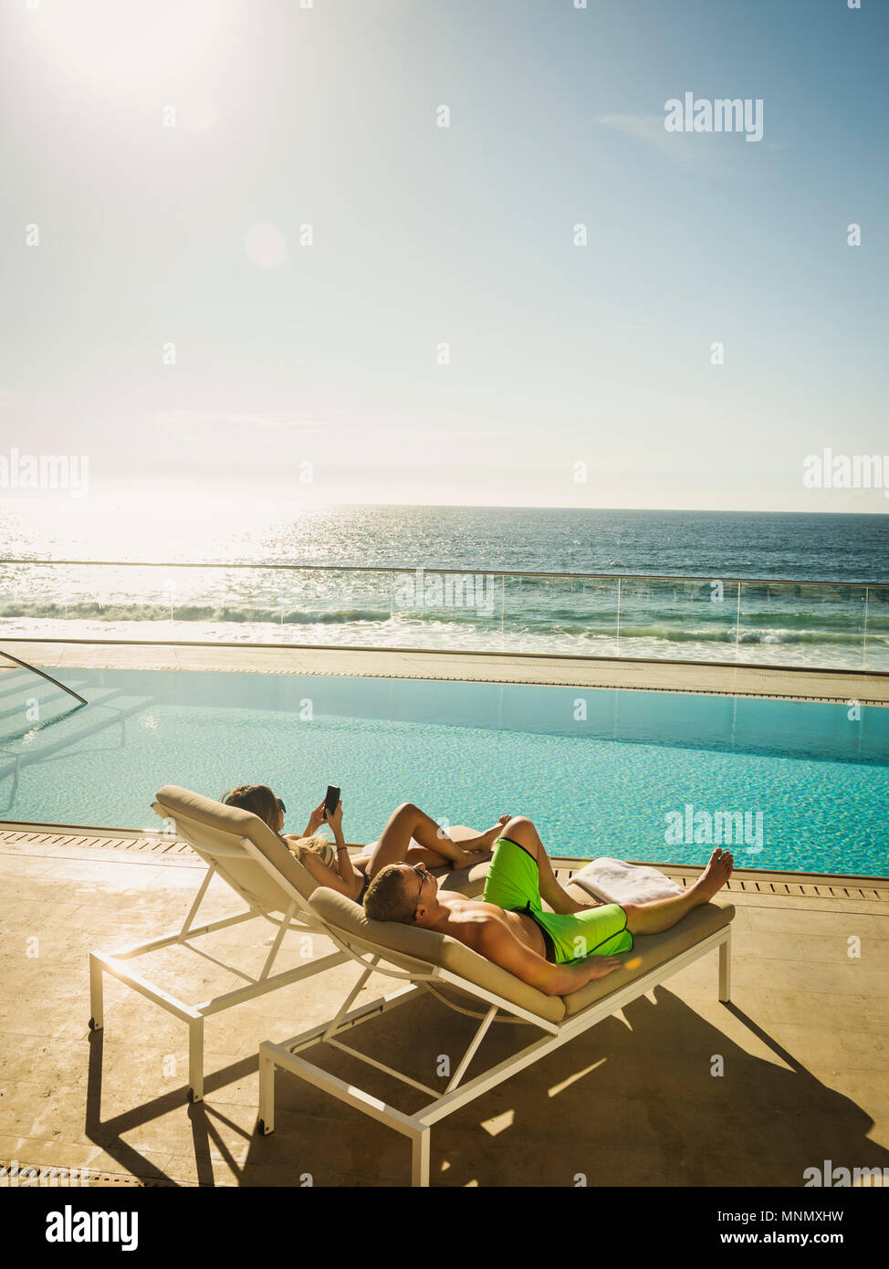 Couple relaxing by swimming pool by ocean Stock Photo