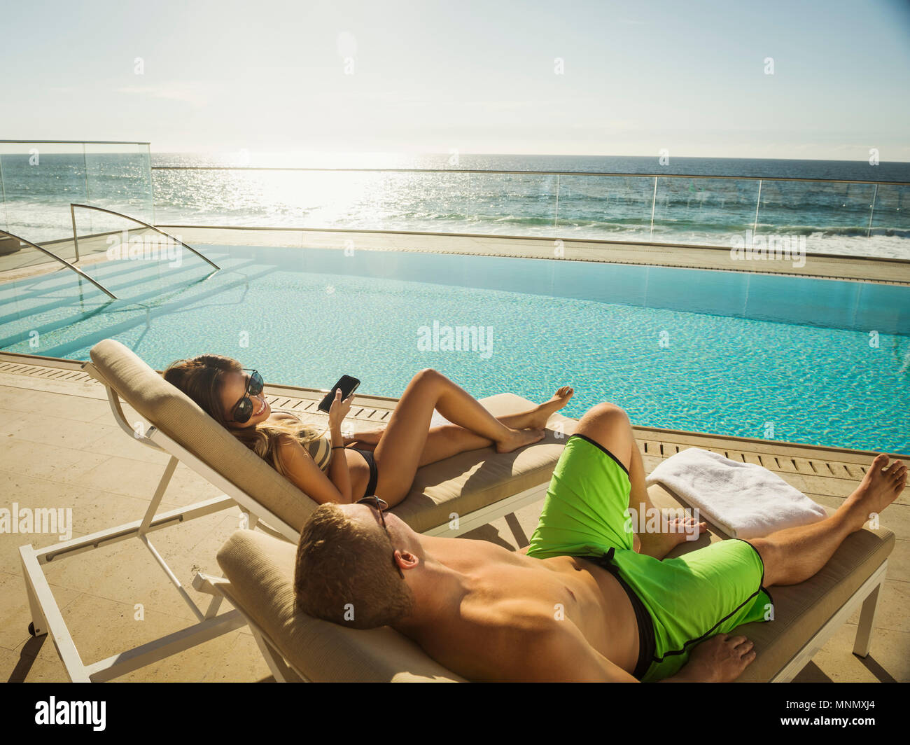 Couple relaxing by swimming pool by ocean Stock Photo