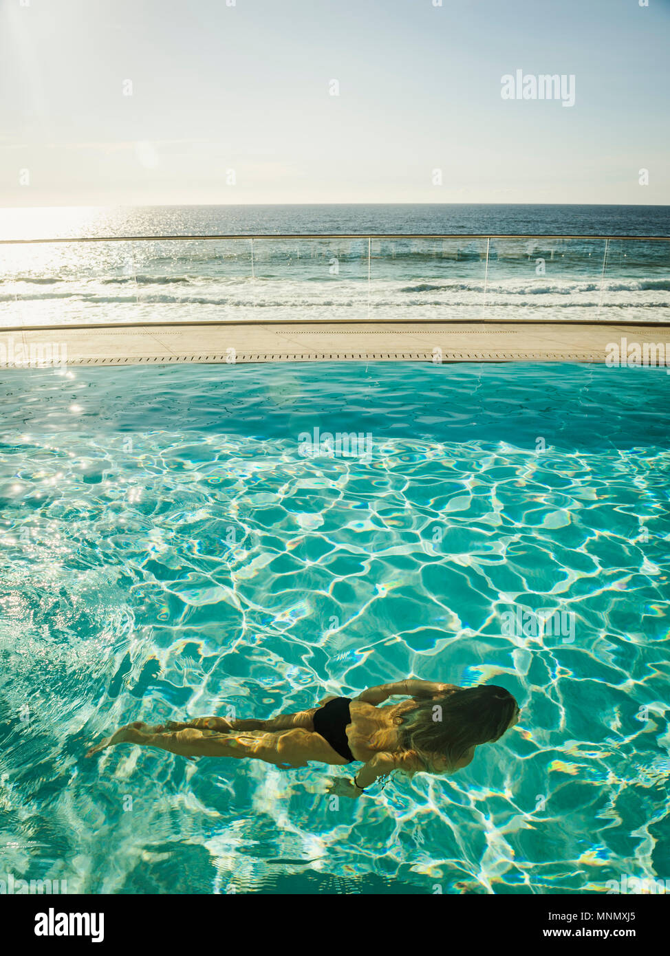 Woman swimming in pool by ocean Stock Photo