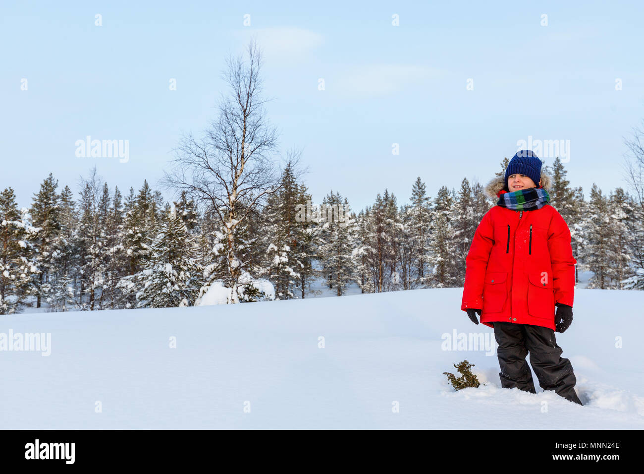 Cute boy in a red parka down jacket outdoors on beautiful winter snowy day Stock Photo