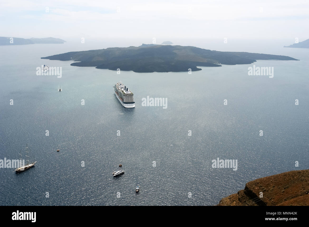 View of a large passenger liner, small ships and a volcanic island in the bay of Santorini, Greece. Stock Photo