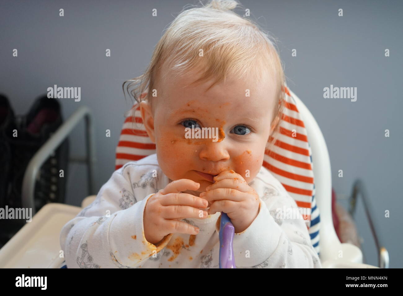Weaning six-month old baby girl in the kitchen with food all over her face Stock Photo