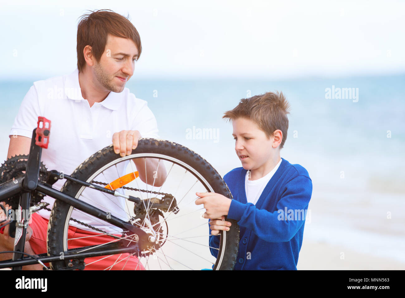 Teenage boy and his father repairing bicycle outdoors at summer Stock Photo