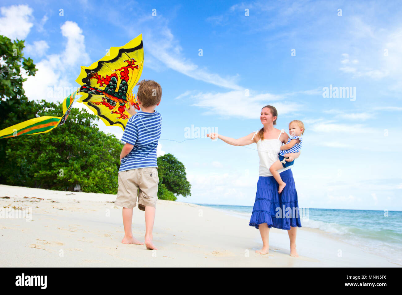 Mother and two kids flying kite on tropical beach. Focus on boy 