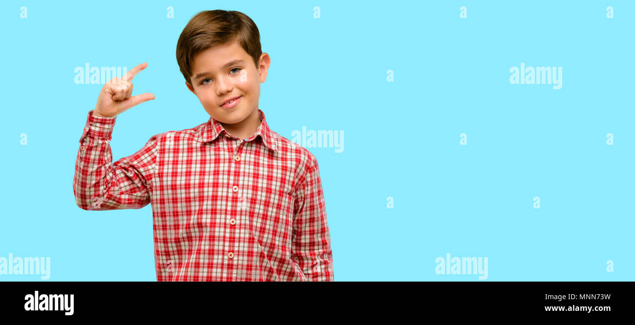 Handsome toddler child with green eyes holding something very tiny, size concept over blue background Stock Photo