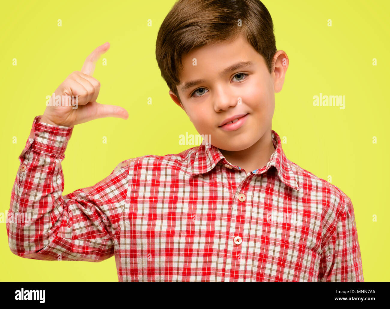 Handsome toddler child with green eyes holding something very tiny, size concept over yellow background Stock Photo