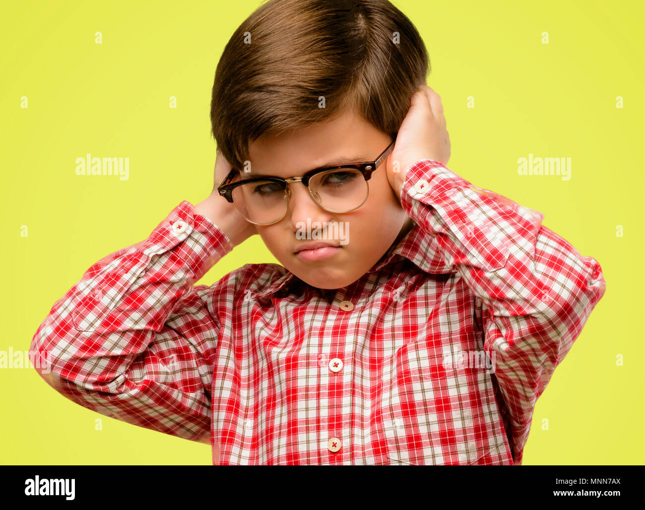 Handsome toddler child with green eyes covering ears ignoring annoying