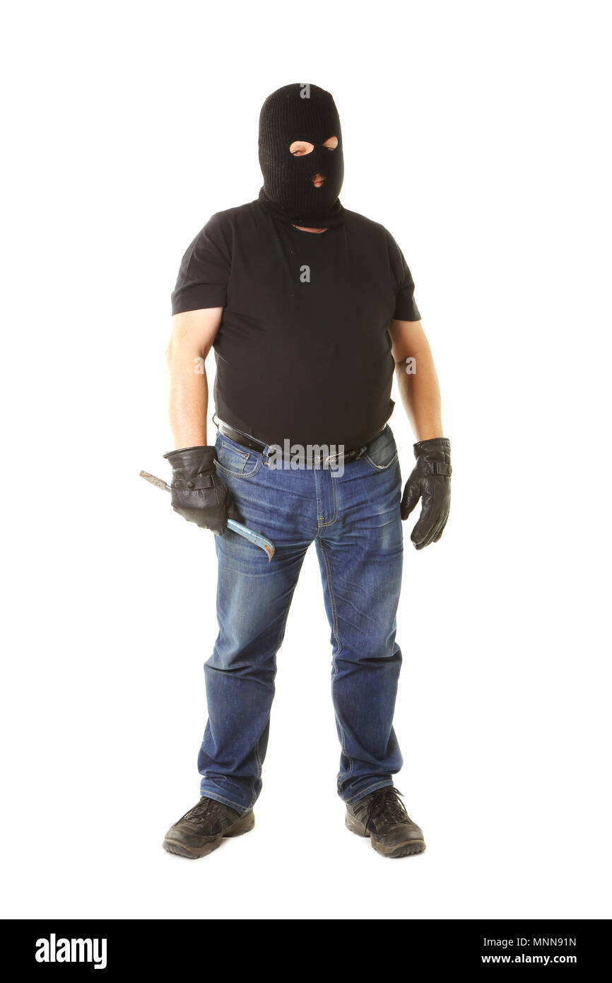 A standing person from the front with black t-shirt, blue jeans masked with a black balaklava holding a crowbar isolated against white background. Stock Photo