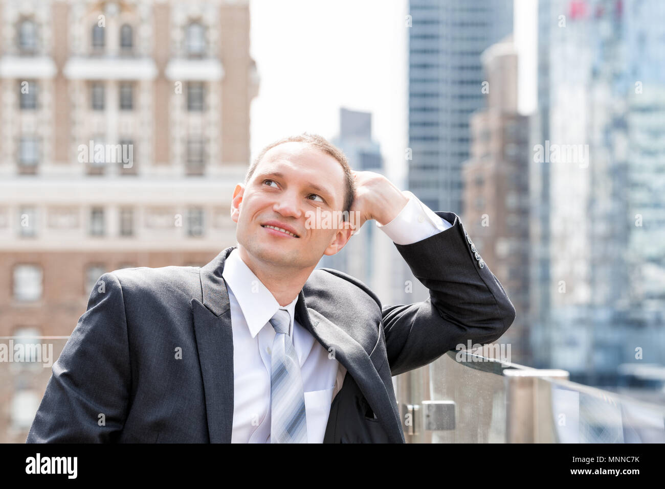 Handsome, attractive young happy smiling businessman closeup face portrait standing in suit, tie, looking up on New York City cityscape skyline in Man Stock Photo