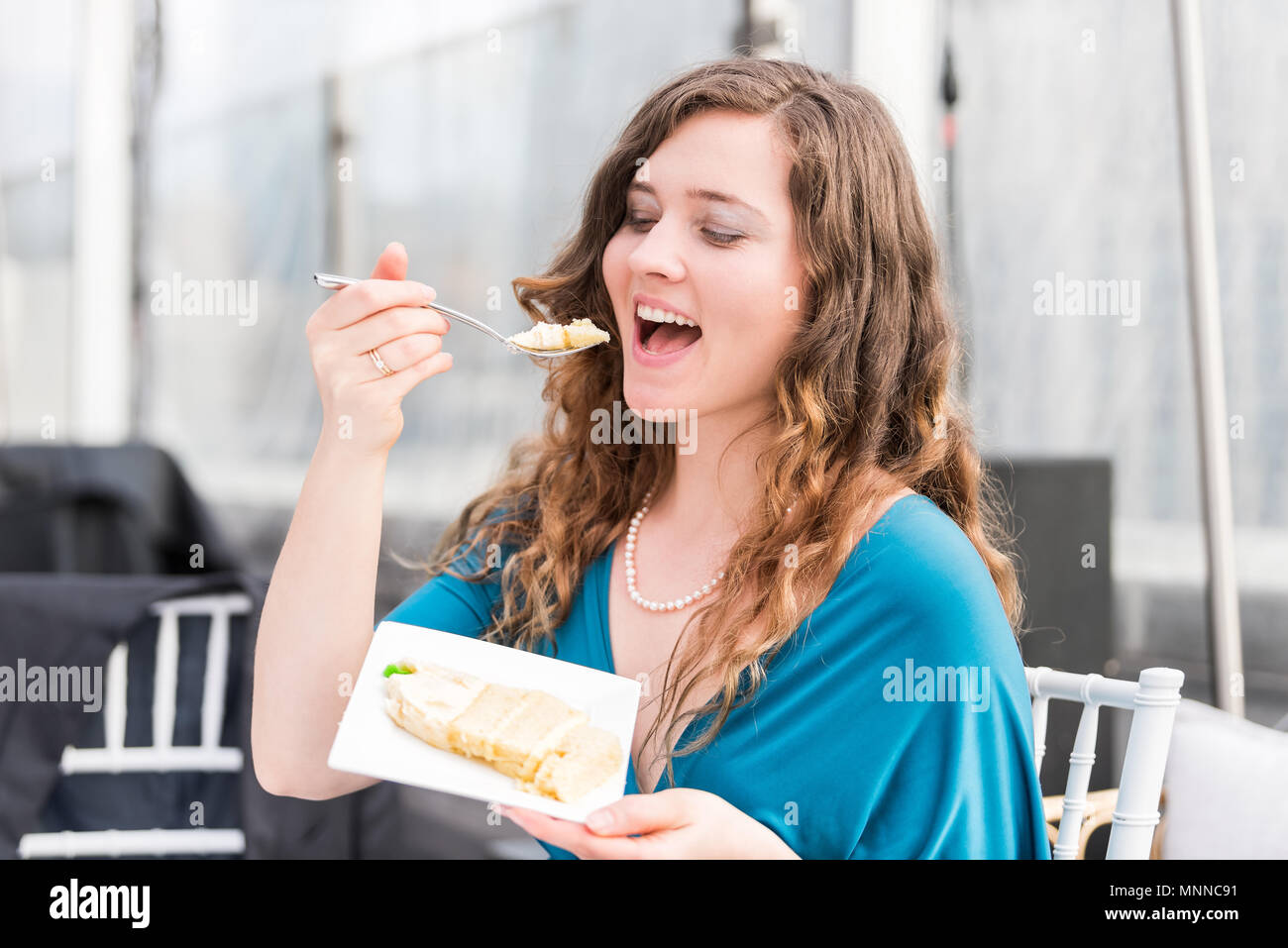 Young happy elegant smiling woman eating cake, open mouth with fork at