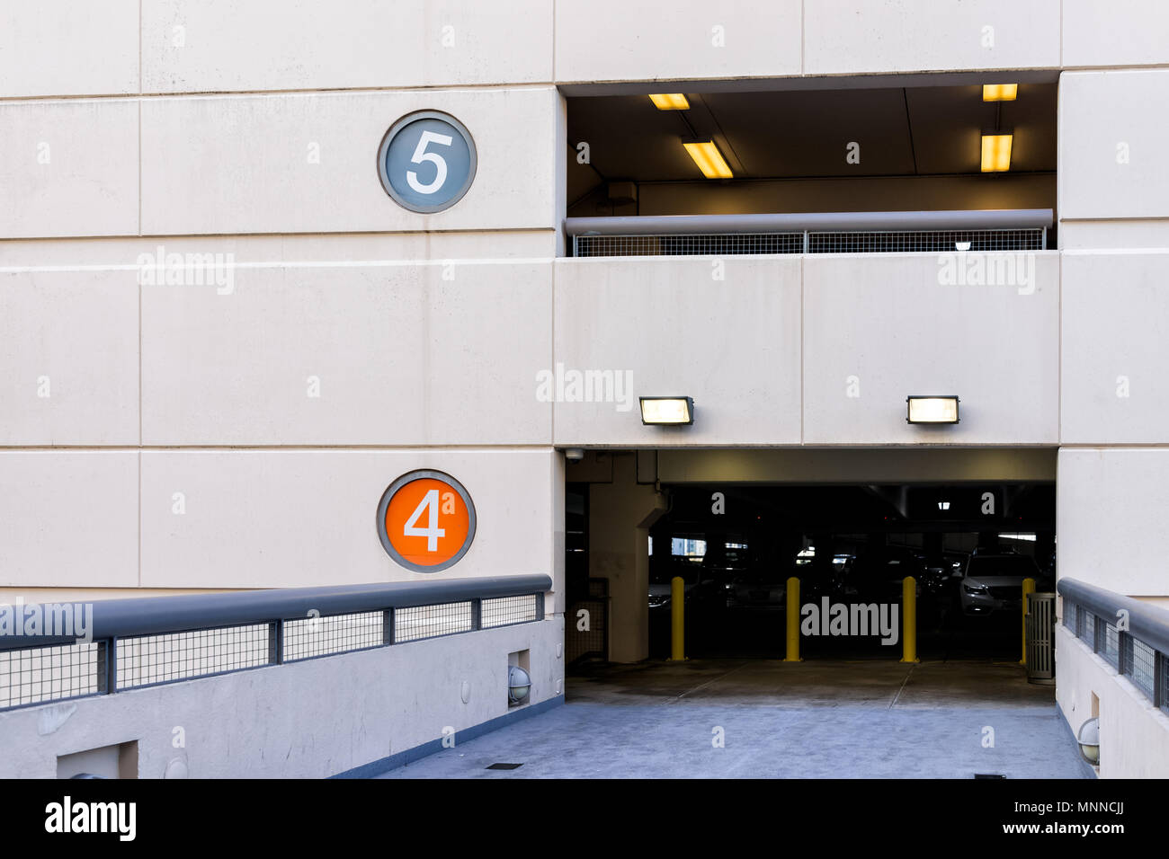 Retail department store mall parking garage with colorful color coded numbers for story level, cars, bridge passage to high building Stock Photo