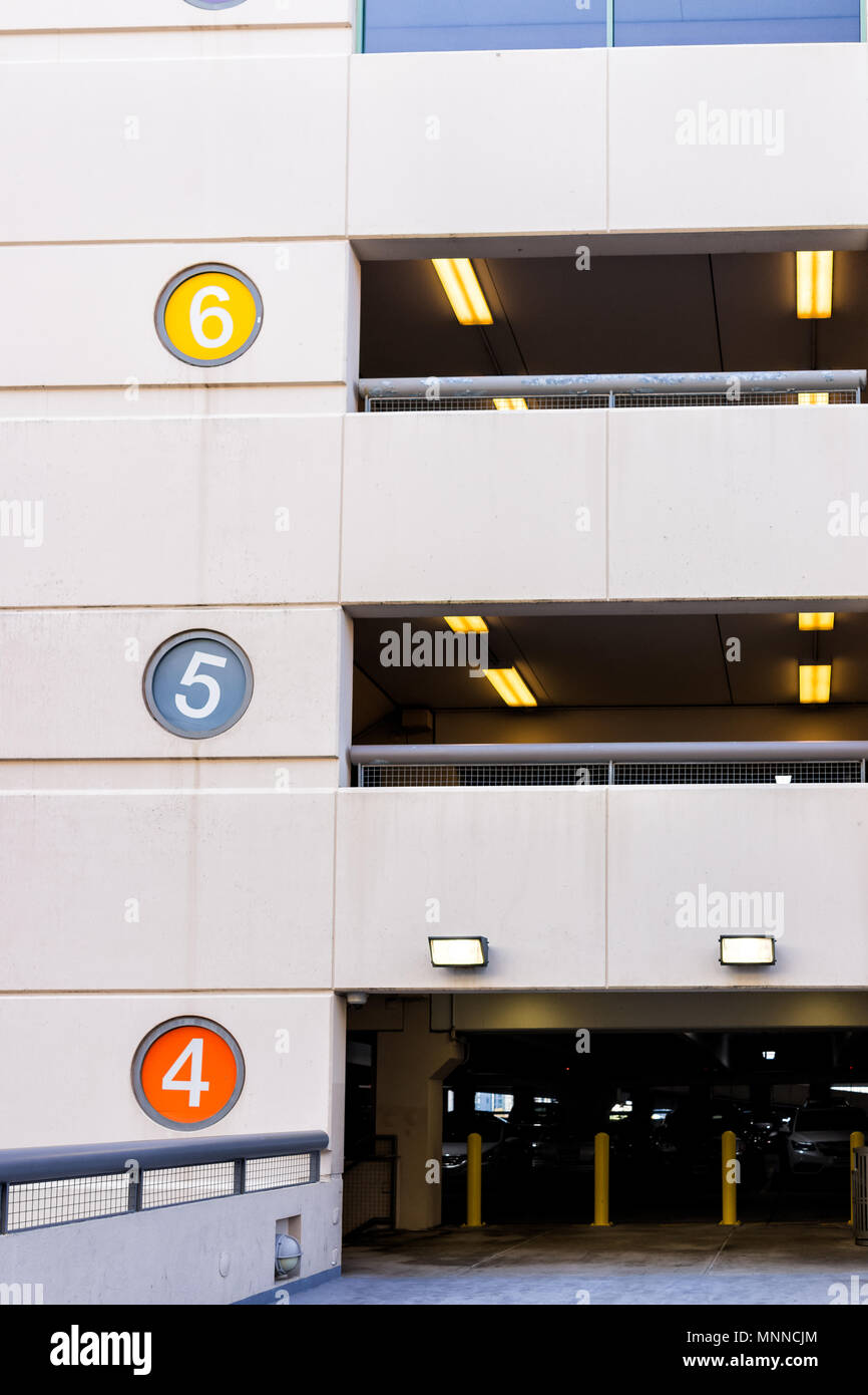 Retail department store mall parking garage vertical view with colorful color coded numbers for story level, cars, bridge passage to high building Stock Photo