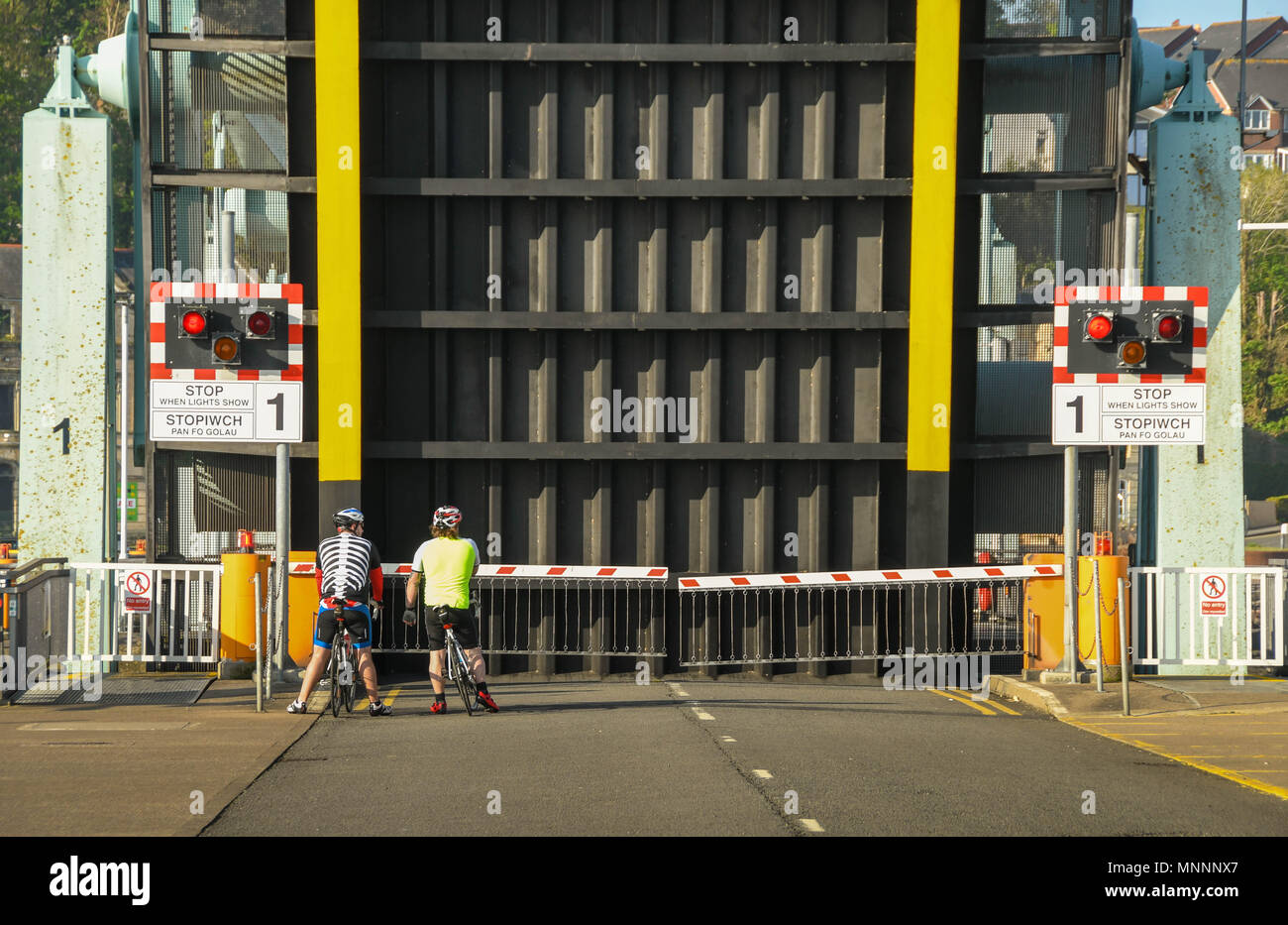 Cyclists wait while a road bridge on the Cardiff Bay barrage is in the raised position. The bridges lift to allow boats to pass into the locks Stock Photo