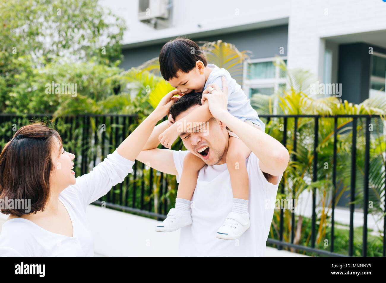 Cute Asian father piggybacking his son along with his wife in the park. Excited family spending time together with happiness Stock Photo