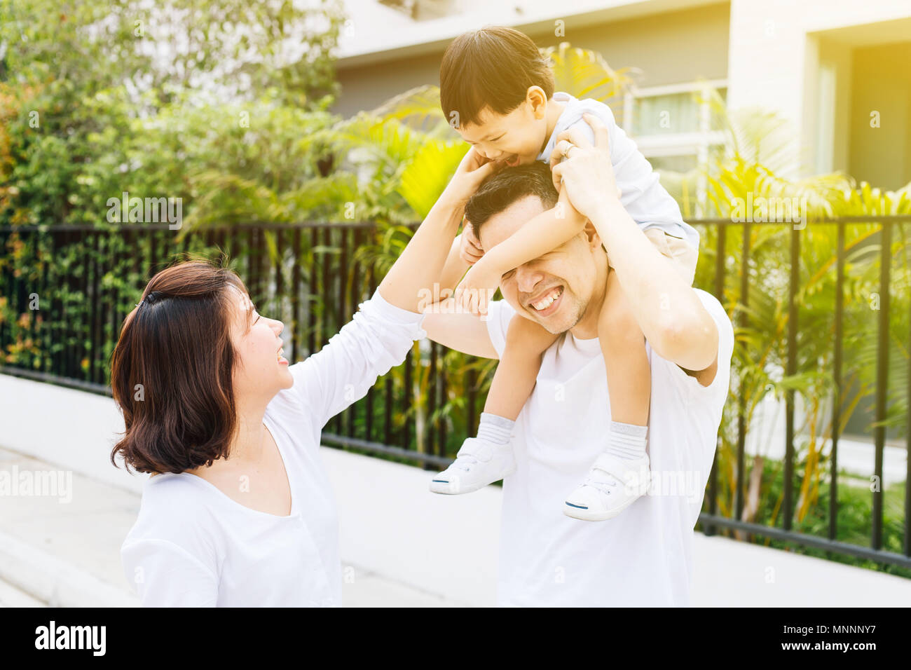 Cute Asian father piggybacking his son along with his wife in the park. Excited family spending time together with happiness Stock Photo